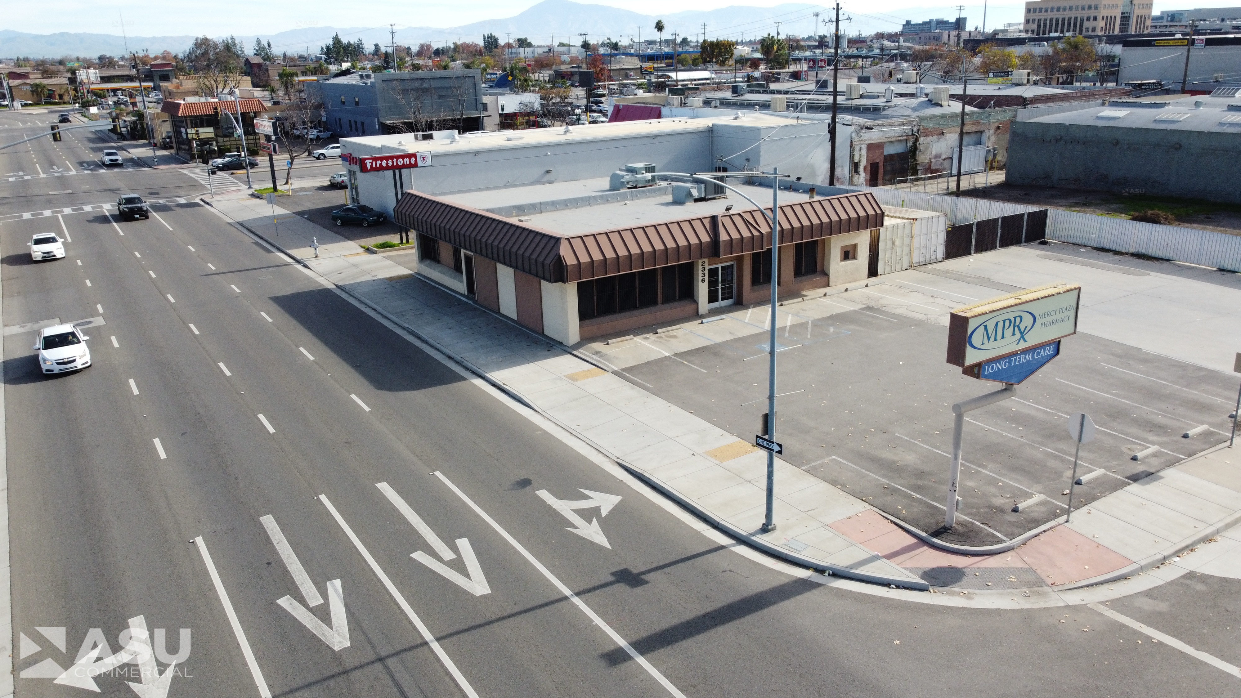 One-story commercial building with brown awning and pole sign on a corner lot beside a wide street