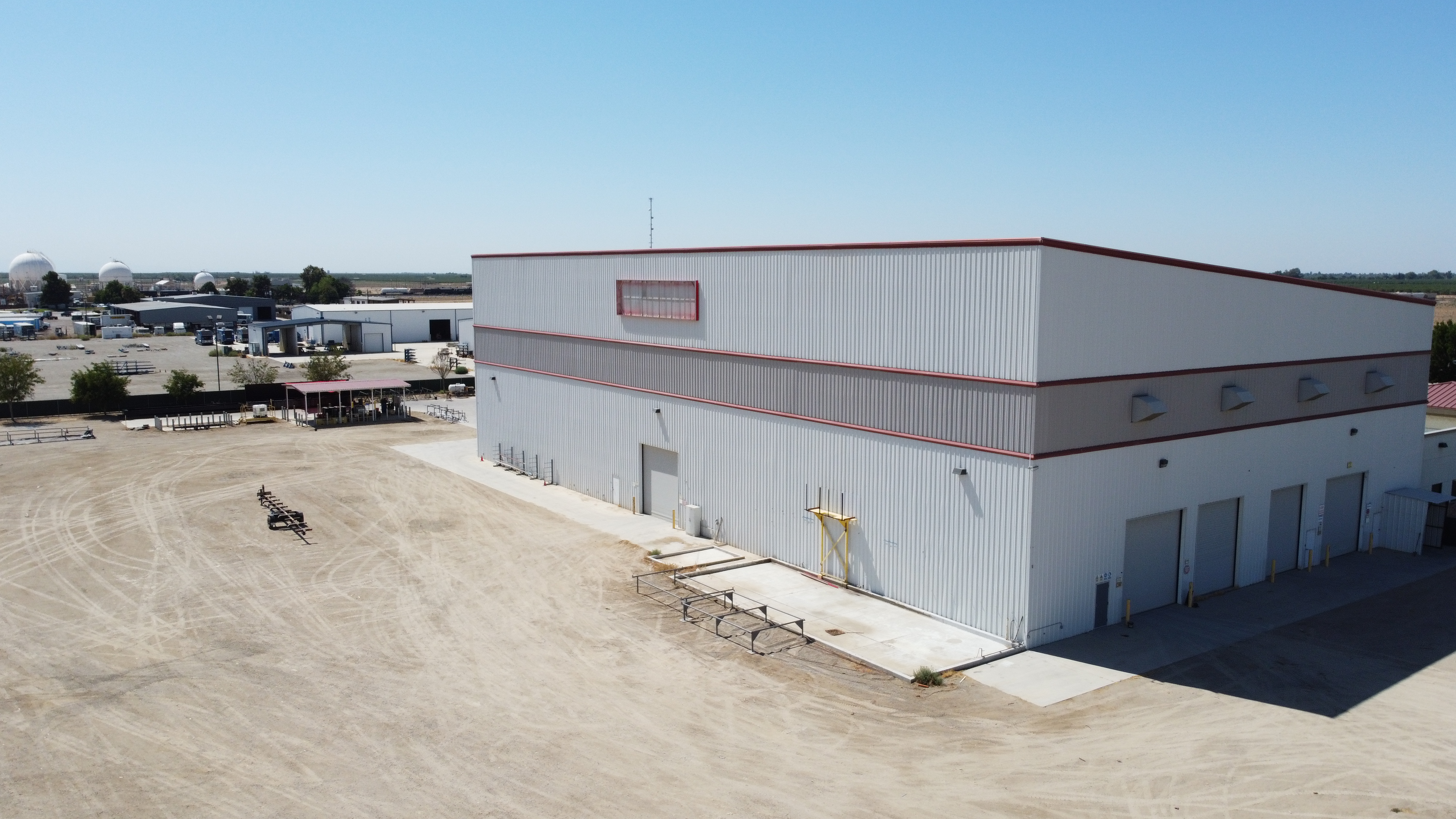 Aerial view of the long side wall of a metal industrial building and a large open dirt yard