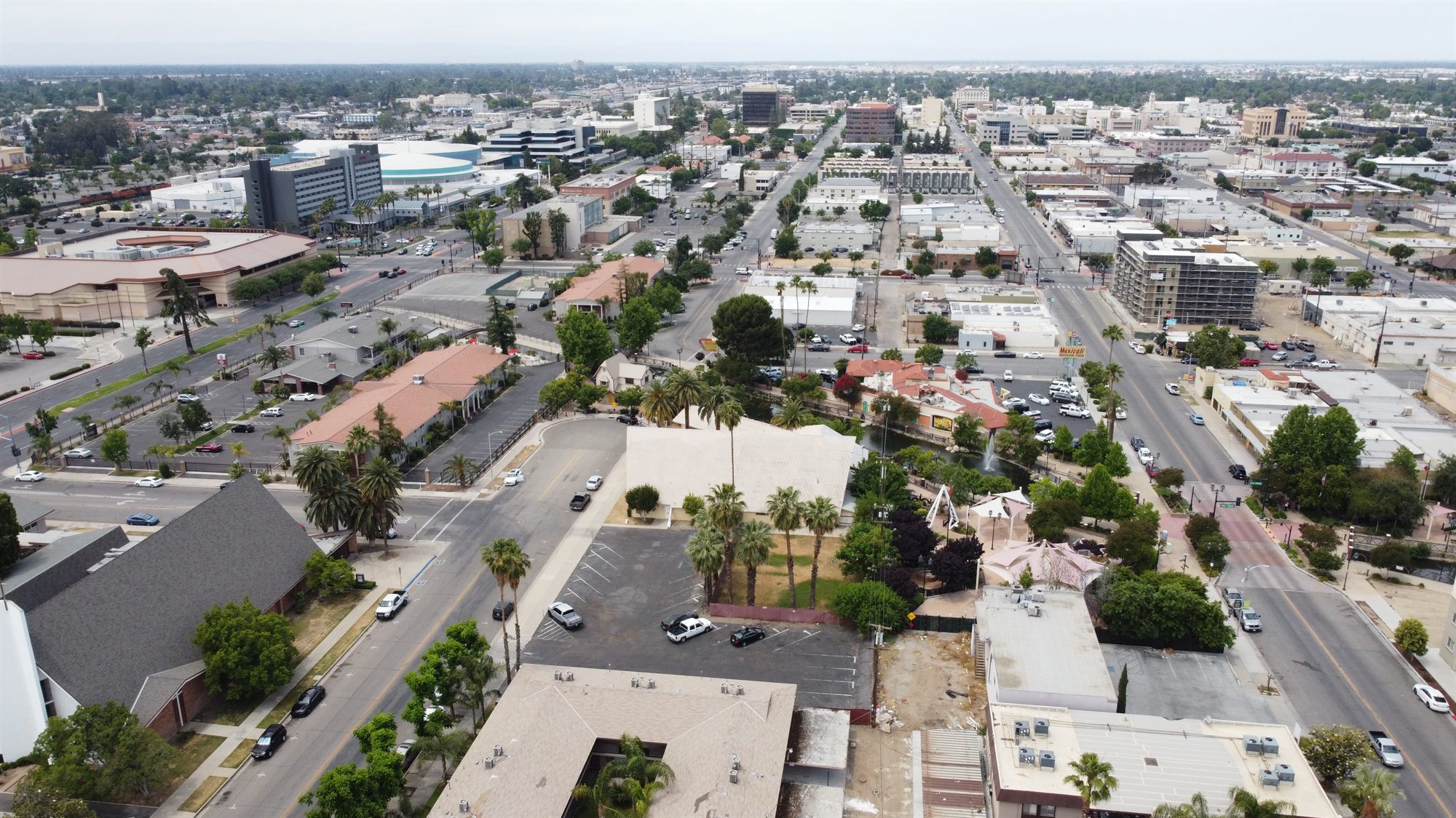 Aerial view across a downtown district of low-rise buildings, parking lots, a pond and a hotel tower