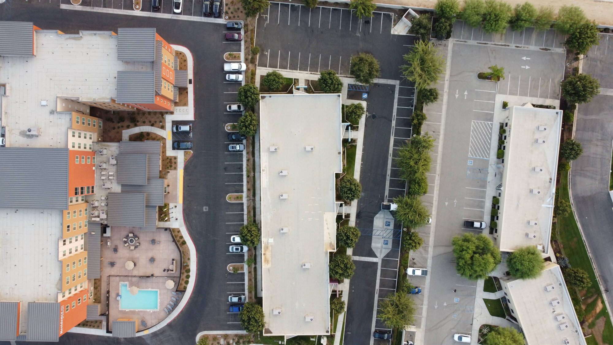 Top-down aerial of a flat-roofed office building, parking lots and a neighboring complex