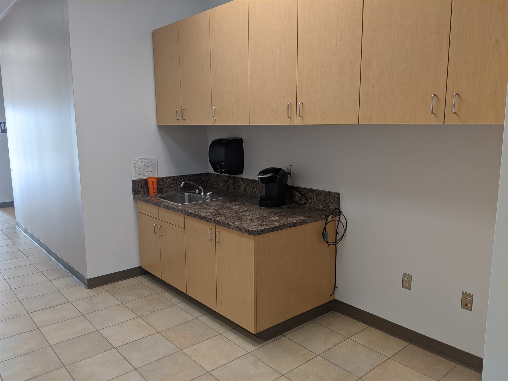 Break room with wood cabinets, sink and coffee maker on a tile floor